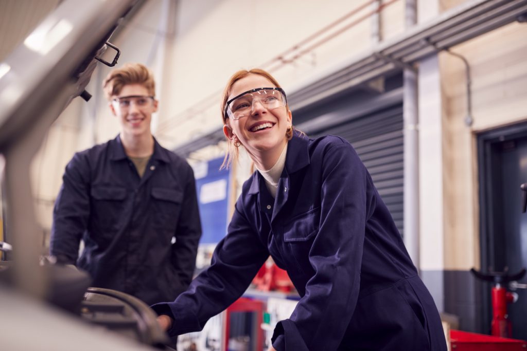 Male and female engineering apprentices with safety goggles and boiler suits smiling