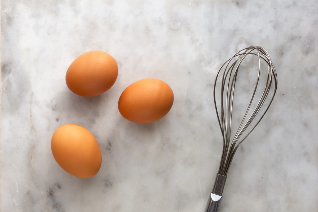 A metal whisk and eggs on marble worktop
